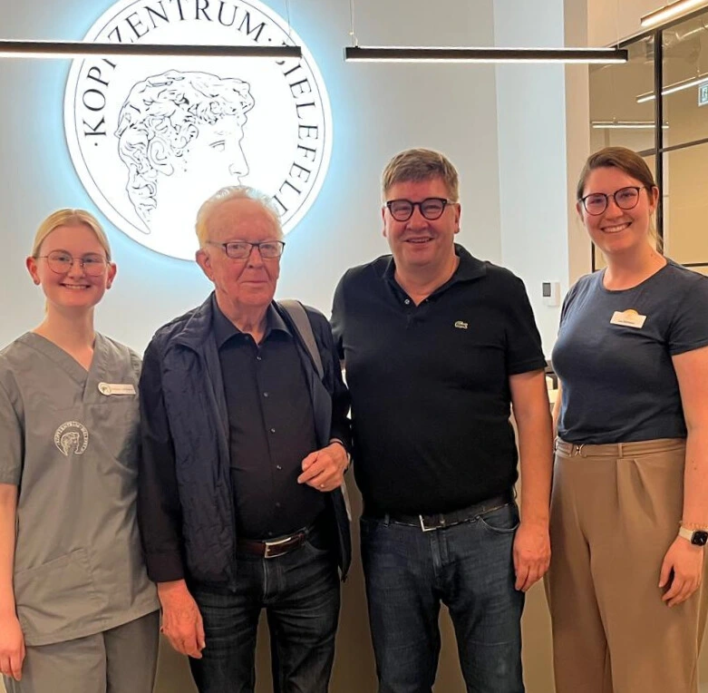Patient und Team vor dem beleuchteten Logo des Kopfzentrums Bielefeld